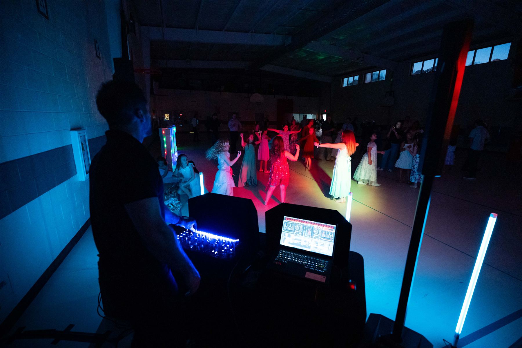 A DJ at his setup with colorful light tubes in a dark gym