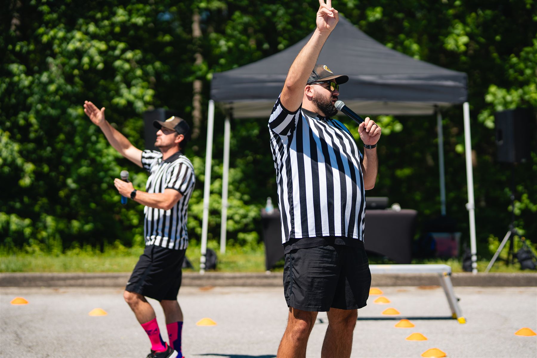 Two emcees in referee shirts with microphones at an outdoor school fundraiser