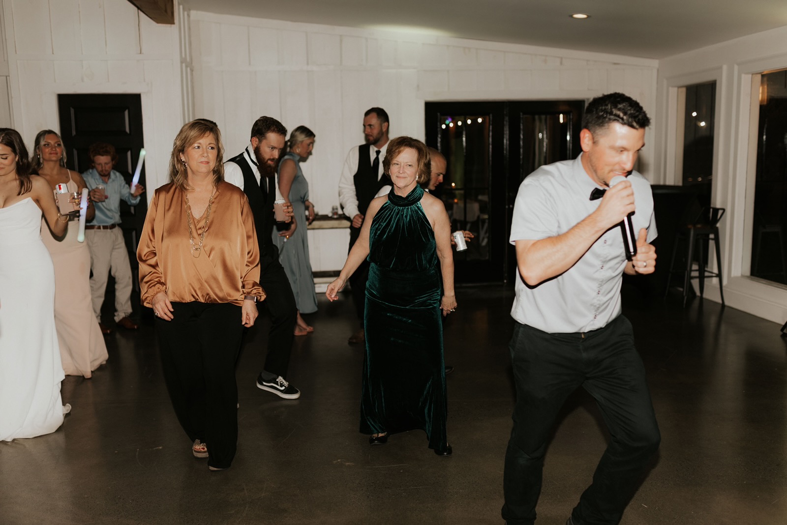 A DJ with a microphone leading wedding guests in a dance